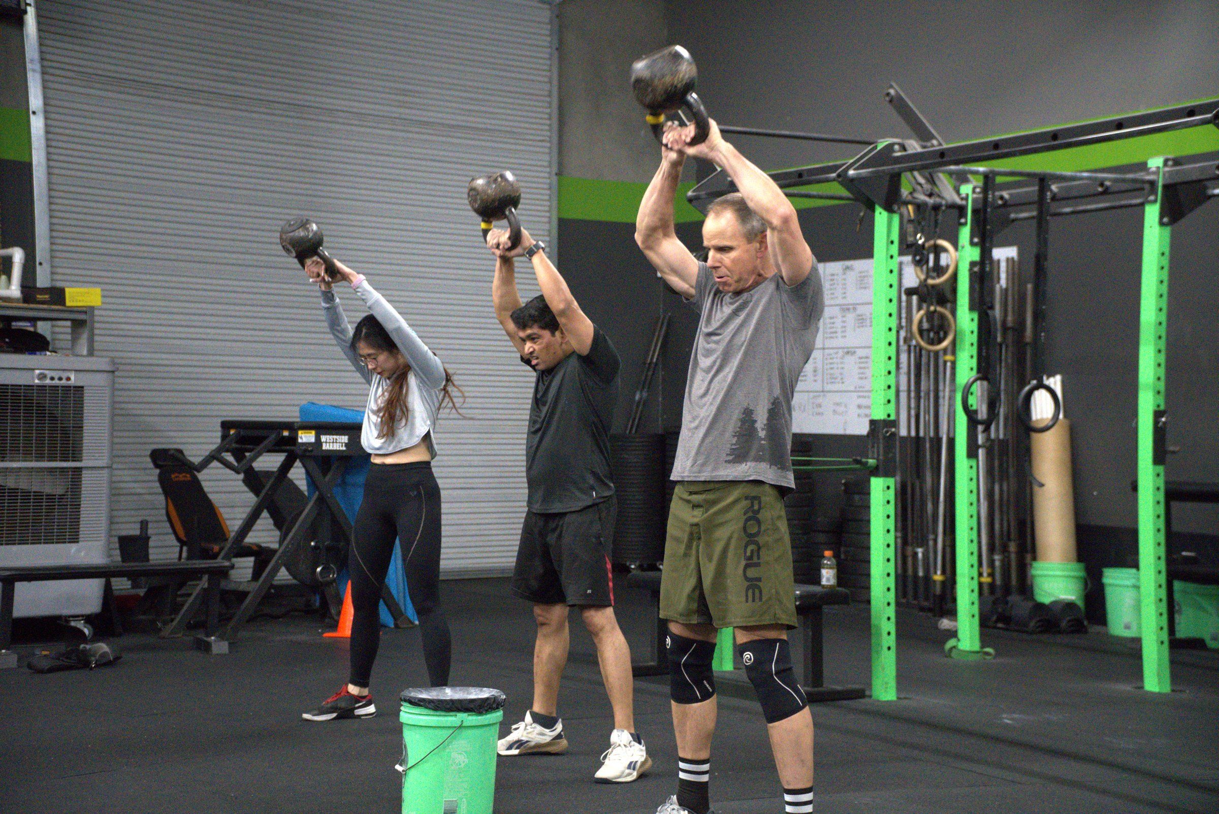 Three members pressing kettlebells overhead together in a group class at EDHFIT