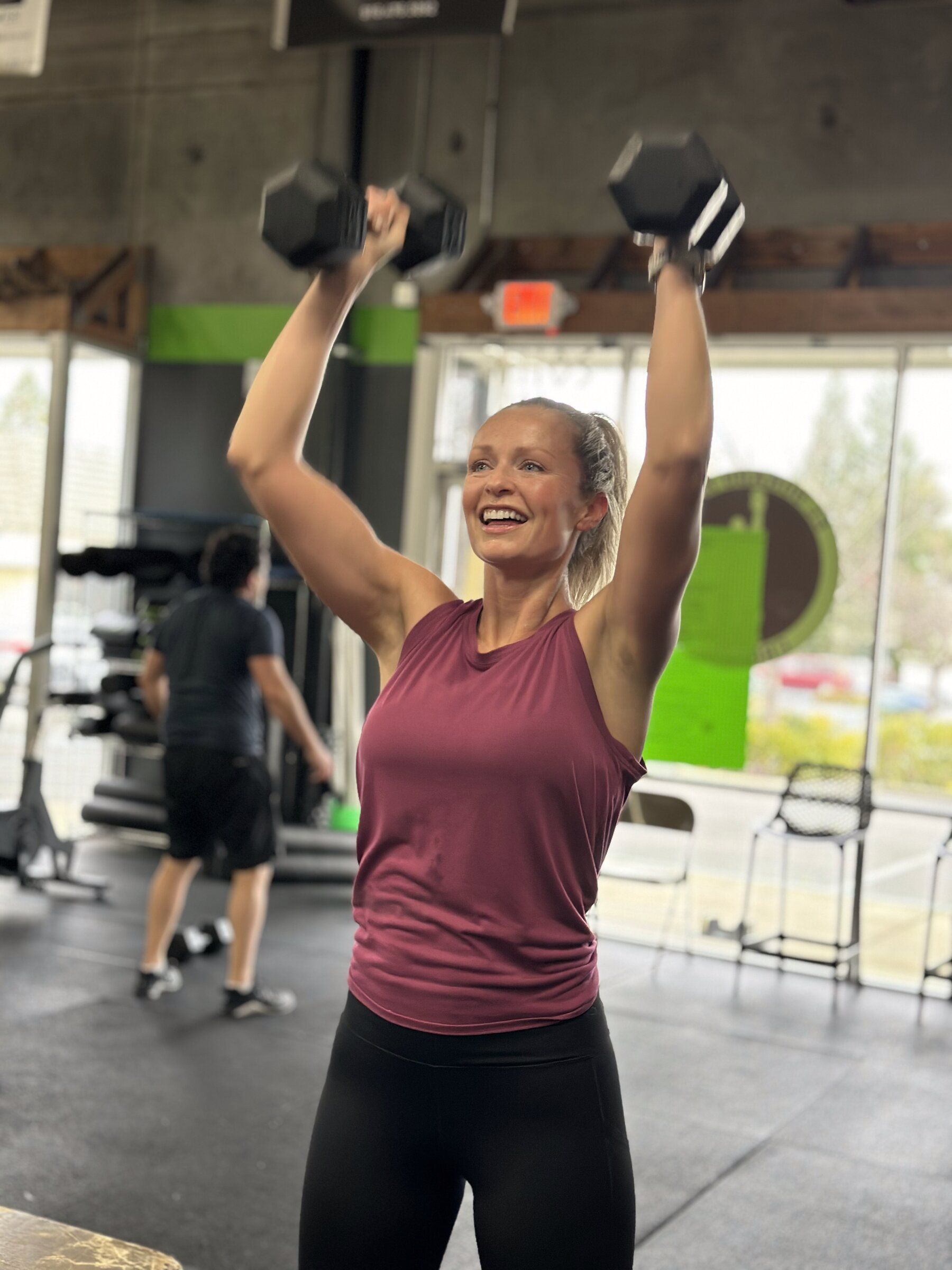 Smiling member pressing dumbbells overhead during a class at EDHFIT